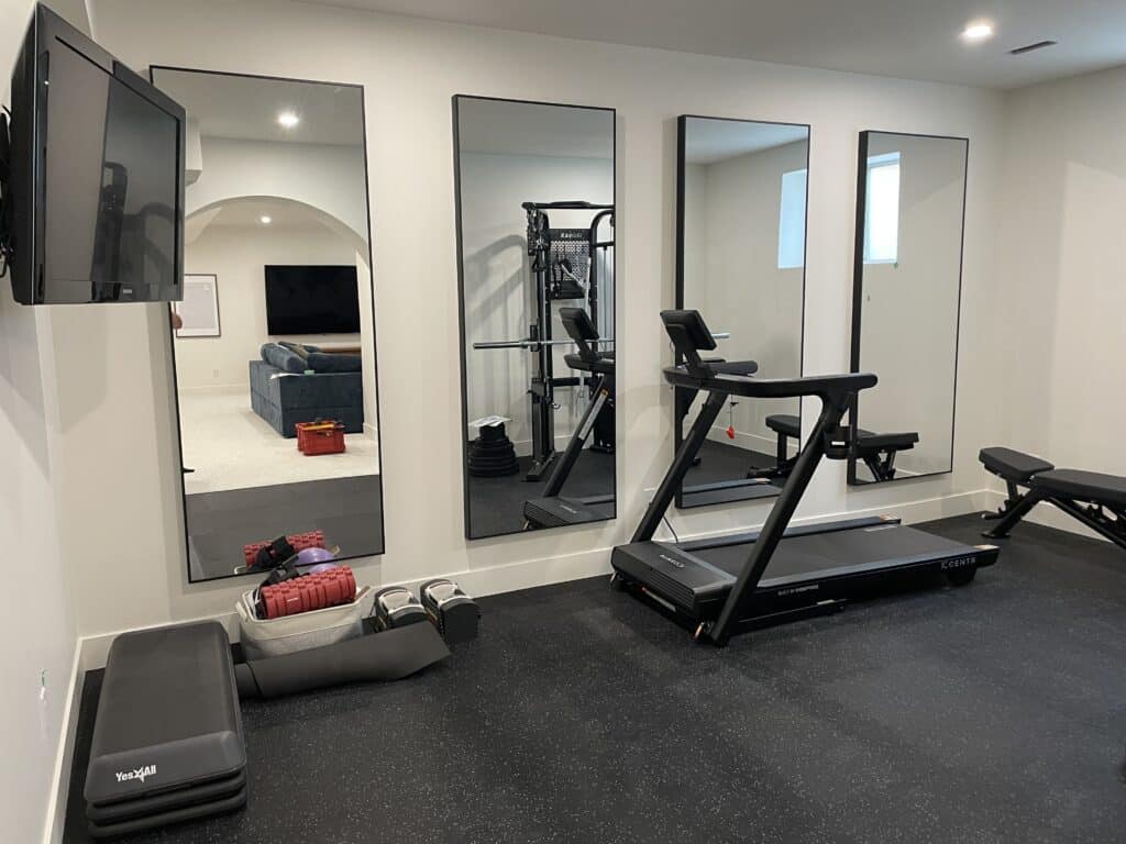 Finished Calgary basement home gym with rubber flooring, full-height mirrors and cardio equipment