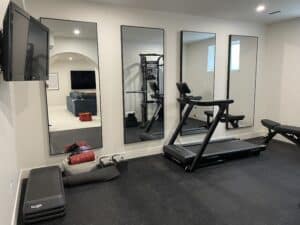 Finished Calgary basement home gym with rubber flooring, full-height mirrors and cardio equipment
