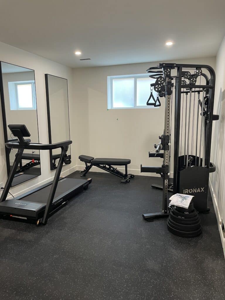 Finished basement home gym in Calgary with treadmill, strength equipment and mirrored wall